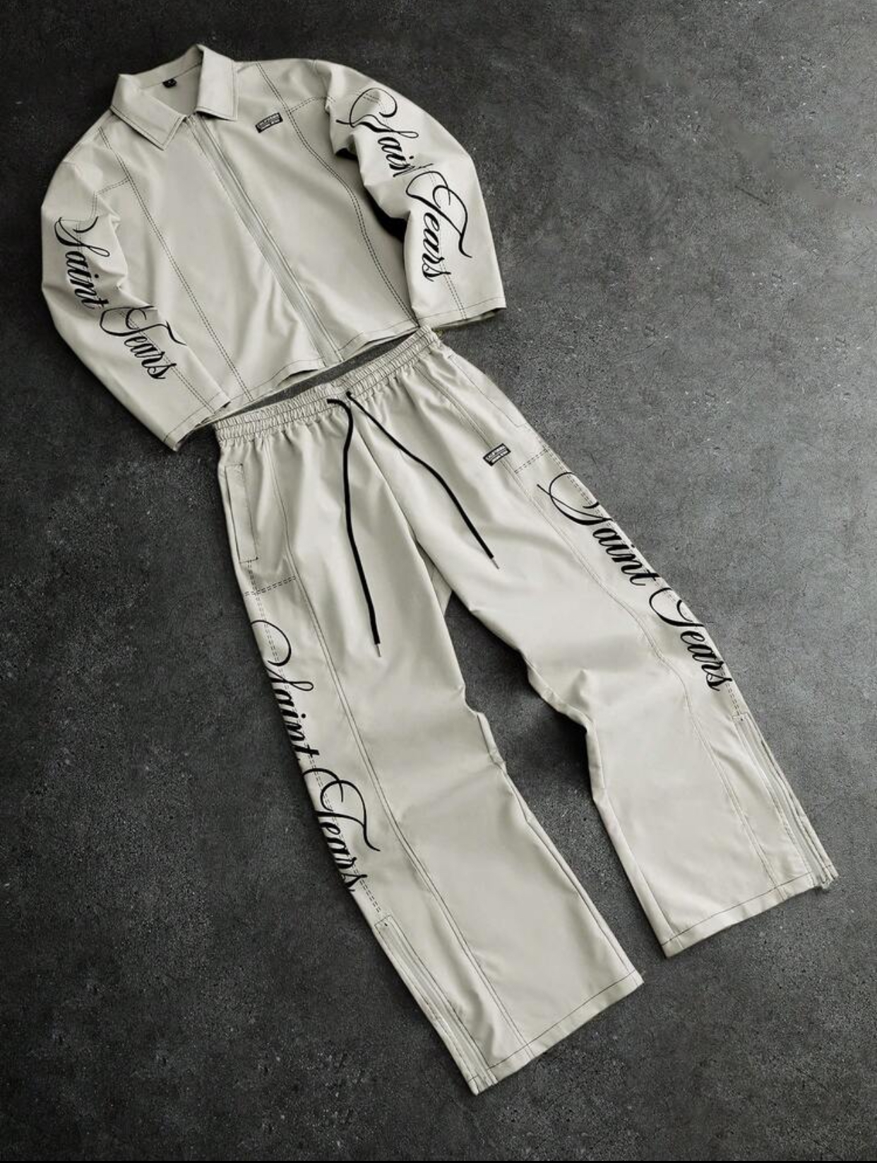 Premium Off-White Cream Structured Faux-Leather Zippered Track Jacket and Matching Wide-Leg Adjustable Drawstring Track Pants Two-Piece Co-ord Streetwear Set Featuring Intricate Contrast Topstitching and Elegant Vertical Black Calligraphy "Saint Tears" Script Graphic Embroidery 2