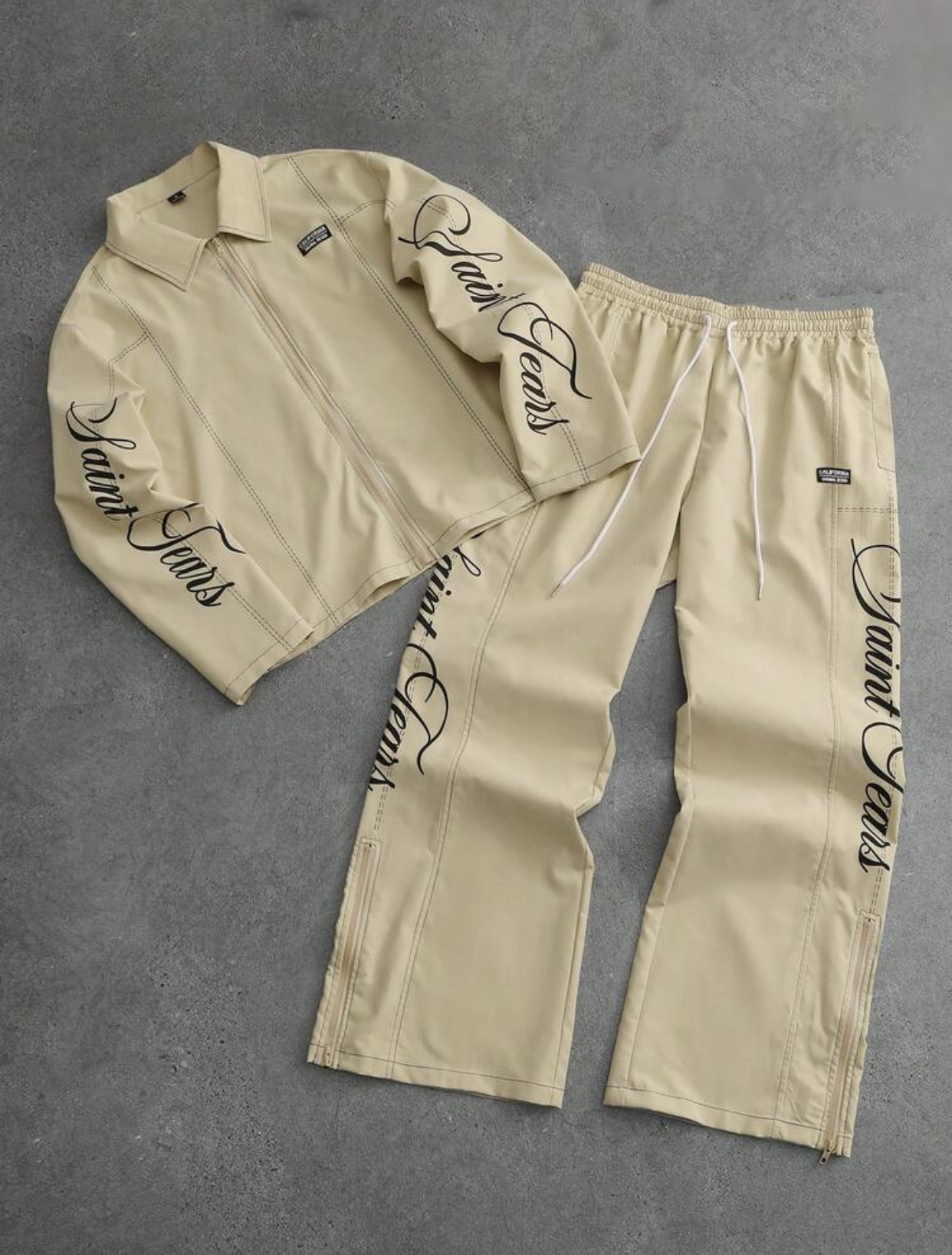 Premium Off-White Cream Structured Faux-Leather Zippered Track Jacket and Matching Wide-Leg Adjustable Drawstring Track Pants Two-Piece Co-ord Streetwear Set Featuring Intricate Contrast Topstitching and Elegant Vertical Black Calligraphy "Saint Tears" Script Graphic Embroidery 3
