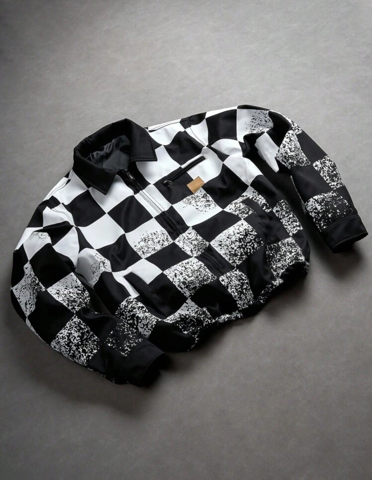 Urban Monochromatic Black and White Oversized Checkerboard Print Zippered Bomber Jacket Featuring a Contrasting Black Pointed Collar, Distressed Grungy Spray-Paint Texturing, and a Premium Minimalist Tan Leather Brand Tab Accent
