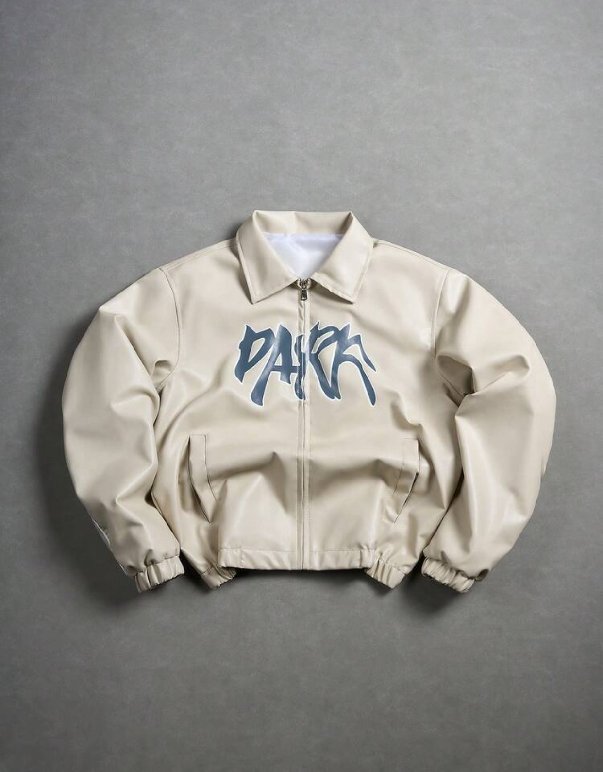 Contemporary Cream-Ivory Supple Faux-Leather Turn-Down Collar Streetwear Blouson Bomber Jacket Configured with Dual Front Slit Welt Pockets, Silver Zipper Hardware, and a Central Abstract Dark Slate Grey-Blue Graffiti "PARK" Bubble Script Graphic 2