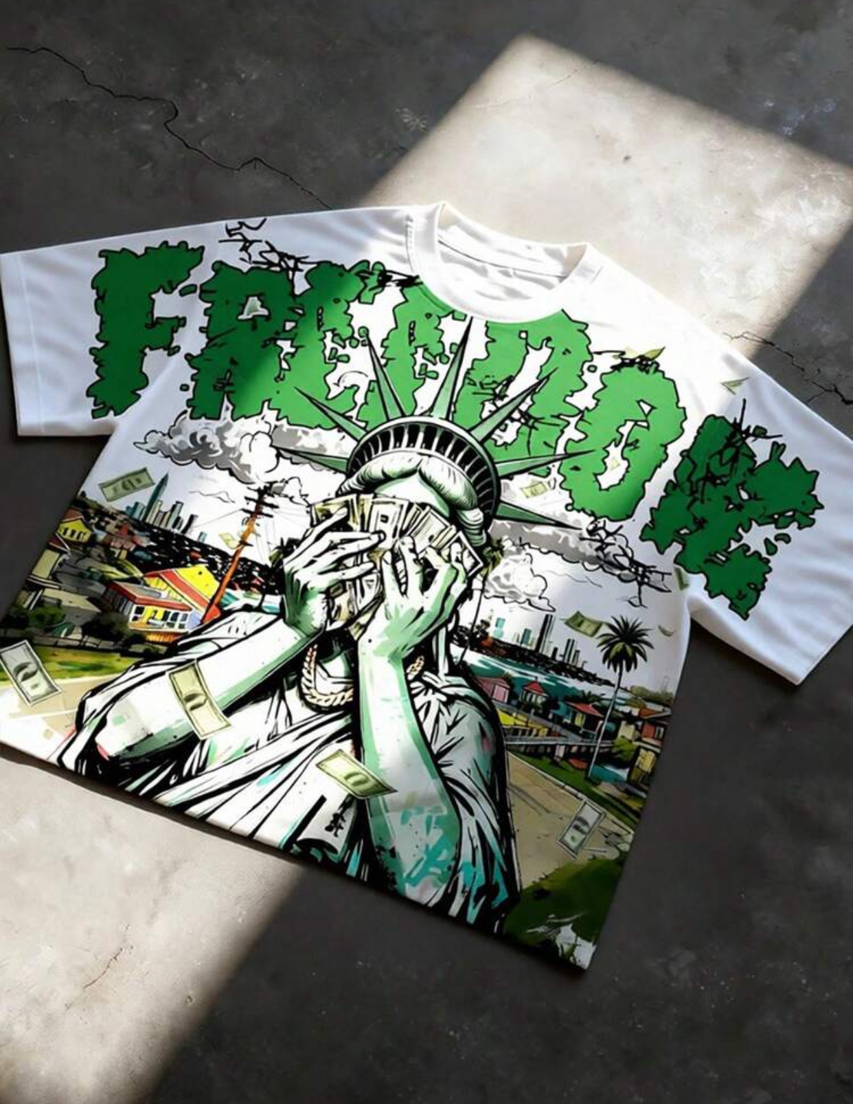 Oversized White Graphic Streetwear T-Shirt Featuring Distressed Bright Green "FREEDOM" Block Letter Typography and a Detailed Illustration of the Statue of Liberty Holding a Fan of US Dollar Bills Against a Flying Money Cityscape Backdrop
