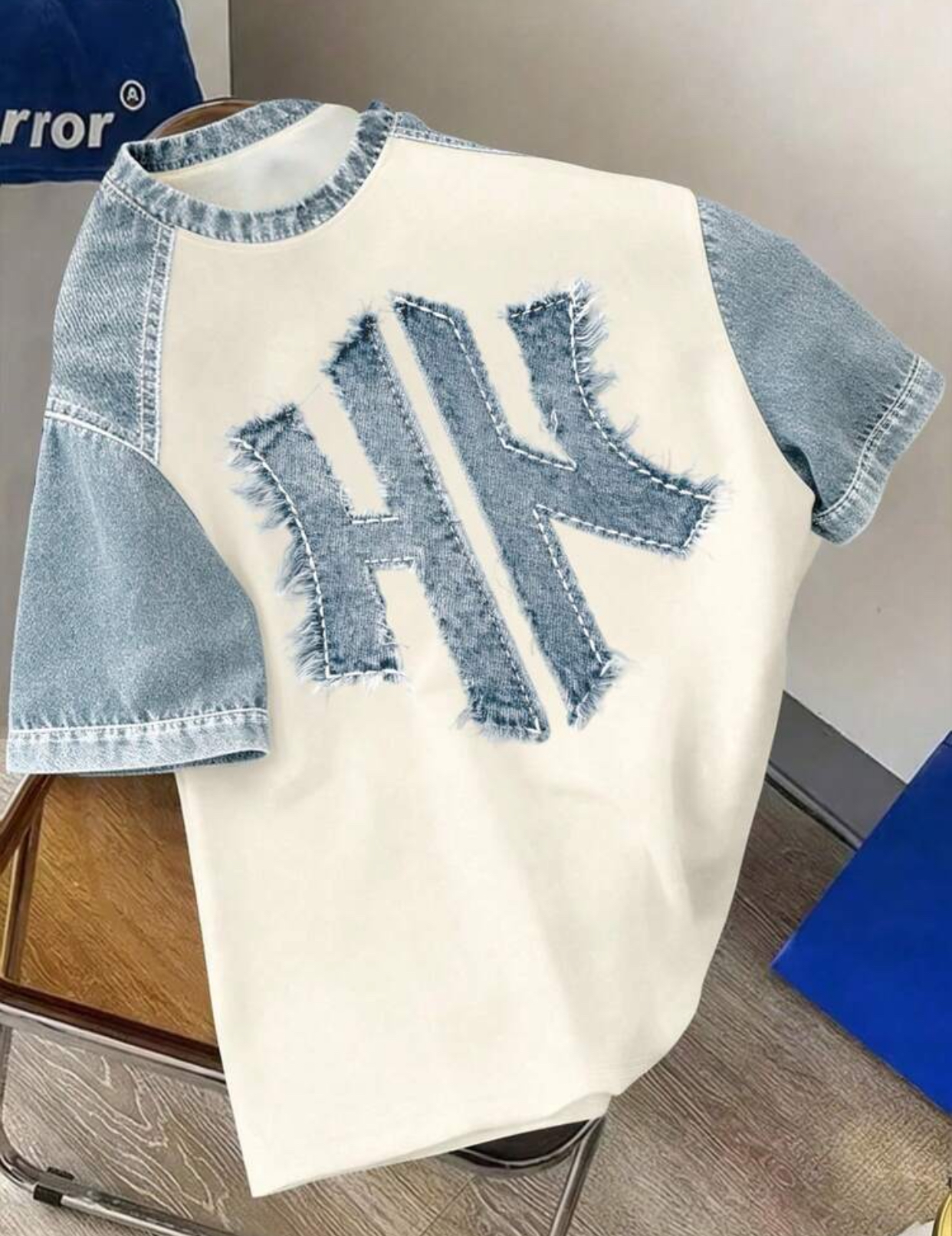 Contemporary Raglan-Style Off-White Streetwear T-Shirt Constructed with Light-Wash Denim Sleeves and an Exaggerated Centered Raw-Edge Frayed Denim "HK" Monogram Applique